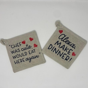 Può includere: Due presine beige con cuori rossi e testo nero. Una presina dice "CHEF WAS cute, WOULD EAT HERE again." L'altra presina dice "Alexa, MAKE DINNER!"