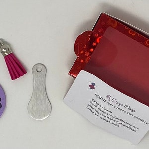 Può includere: Un portachiavi con monogramma viola e nero con un fiocco rosa. Il portachiavi è in una piccola scatola rossa con una finestra trasparente. La scatola ha un'etichetta bianca con il testo "B Maga Maga oggetti fatti a mano con passione Barbara Medola Email barbera.medora@fastweb.it www.etsy.com/shop/LaMagaMago Instagram lemaga_mago"