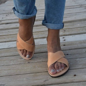 May include: A pair of tan leather sandals with criss-cross straps. The sandals are worn by a person wearing blue jeans.
