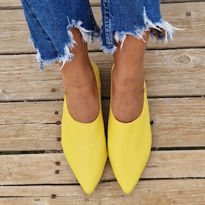 May include: A pair of bright yellow pointed-toe flats with a simple design. The shoes are worn by a person wearing blue jeans.