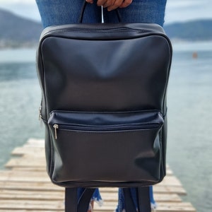 May include: A black leather backpack with a zippered front pocket. The backpack has adjustable straps and a top handle.