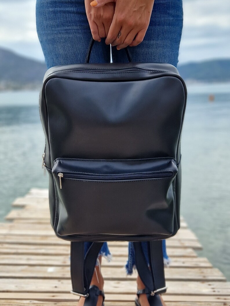 May include: A black leather backpack with a zippered front pocket. The backpack has adjustable straps and a top handle.