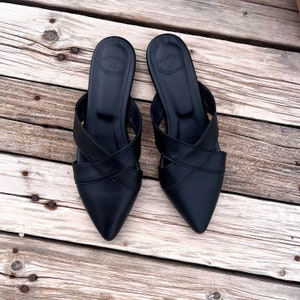 May include: A pair of black leather pointed-toe mules with criss-cross straps. The shoes have a simple design and are made of high-quality leather.