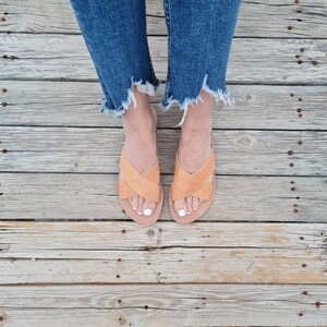 May include: A pair of tan leather sandals with criss-cross straps. The sandals are worn by a person wearing blue jeans.
