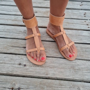 May include: Tan leather sandals with ankle straps and a toe thong. The sandals have a simple design and are perfect for summer.