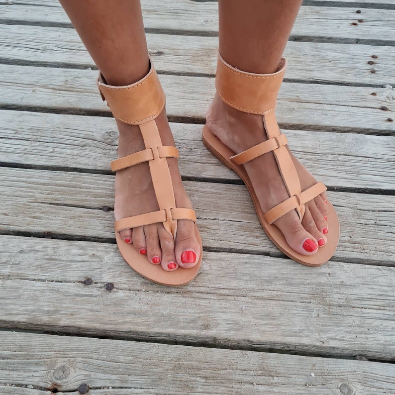 May include: Tan leather sandals with ankle straps and a toe thong. The sandals have a simple design and are perfect for summer.
