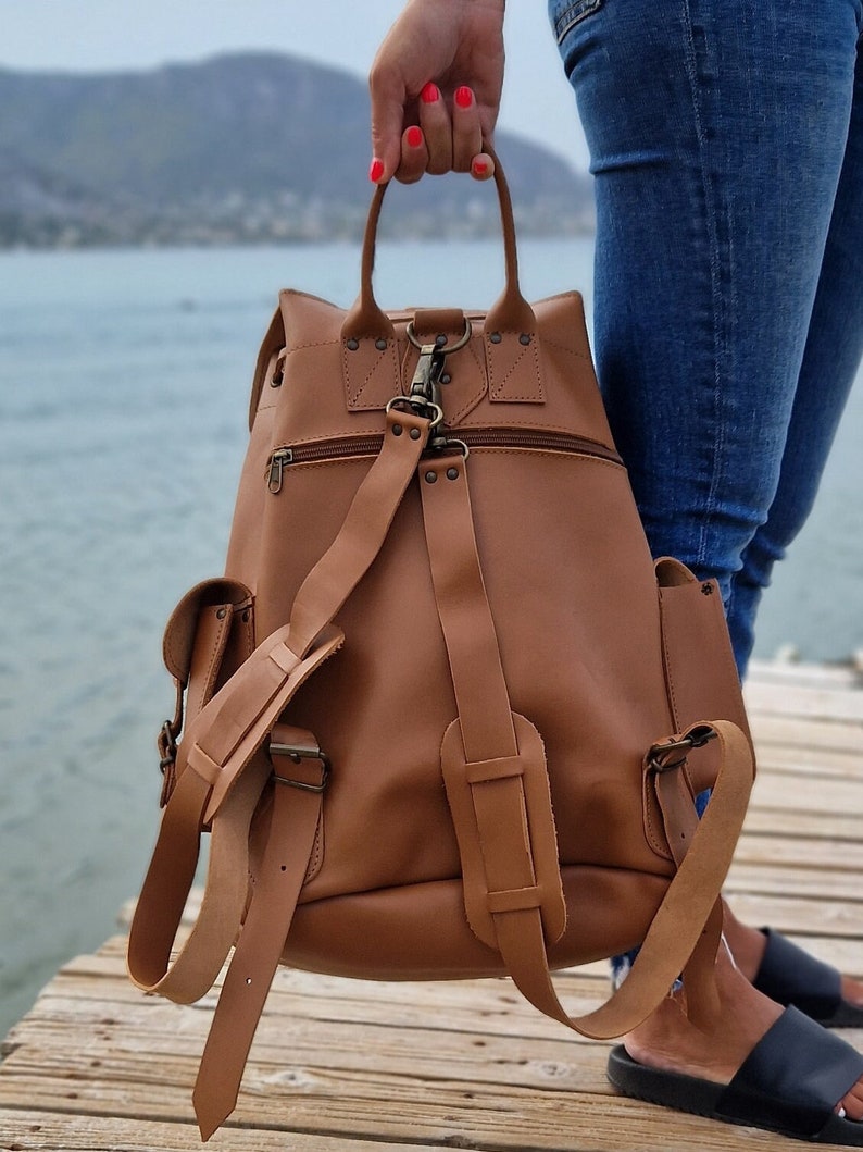 Puede incluir: Una mochila de cuero marr&oacute;n con correas ajustables y varios bolsillos. La mochila tiene un asa superior y un cierre de cremallera.