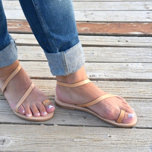 Puede incluir: Un par de sandalias de cuero marr&oacute;n claro con un dise&ntilde;o de tiras cruzadas. Las sandalias se llevan en los pies de una mujer, y las tiras son visibles en la parte superior del pie.