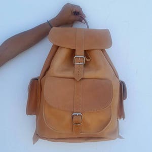Puede incluir: Una mochila de cuero marr&oacute;n con dos bolsillos delanteros y un cierre de hebilla.