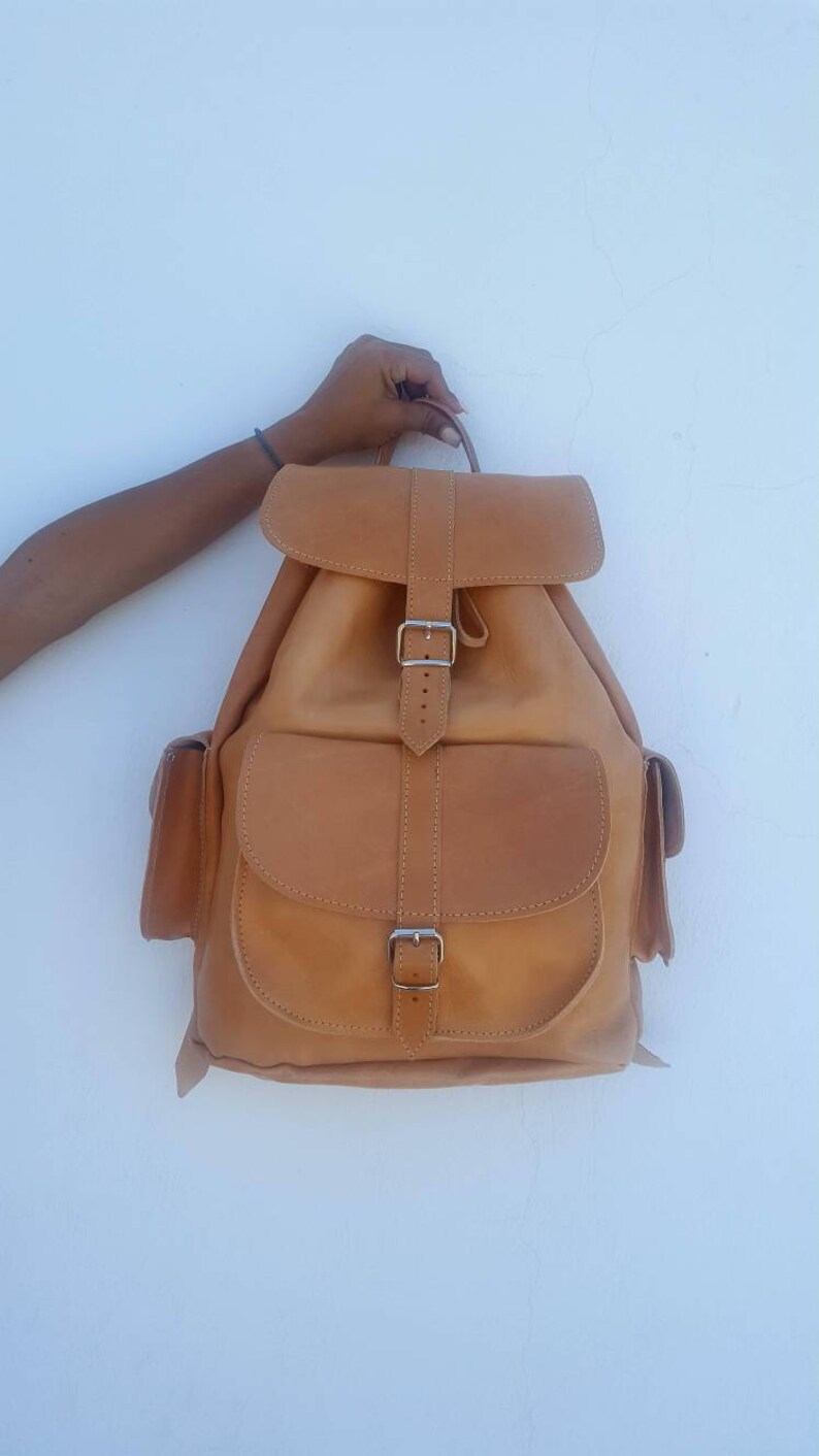 Puede incluir: Una mochila de cuero marr&oacute;n con dos bolsillos delanteros y un cierre de hebilla.