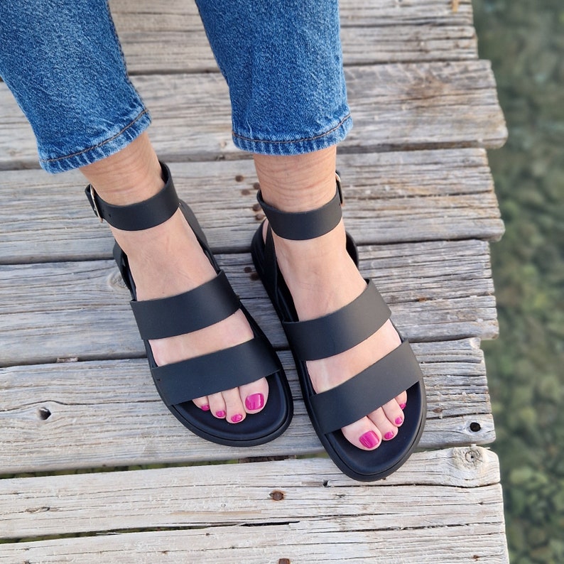 May include: A pair of black leather sandals with two straps across the foot and an ankle strap. The sandals have a chunky platform sole.