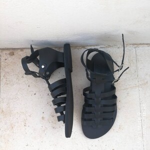 May include: A pair of black leather gladiator sandals with a criss-cross strap design.