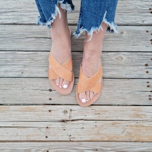 May include: A pair of tan leather sandals with criss-cross straps. The sandals have a simple design and are perfect for summer.