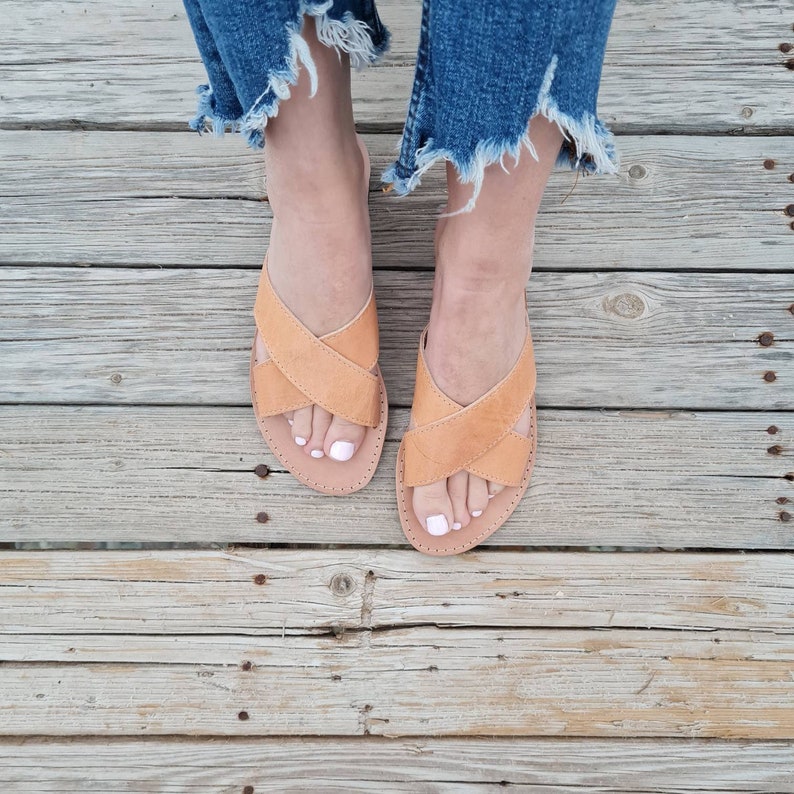 May include: A pair of tan leather sandals with criss-cross straps. The sandals have a simple design and are perfect for summer.