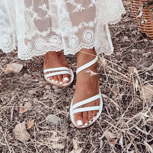 May include: White leather sandals with multiple straps. The sandals have a simple design and are perfect for summer.