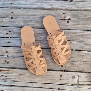 May include: A pair of tan leather sandals with a woven strap design. The sandals have a flat sole and are open-toe.