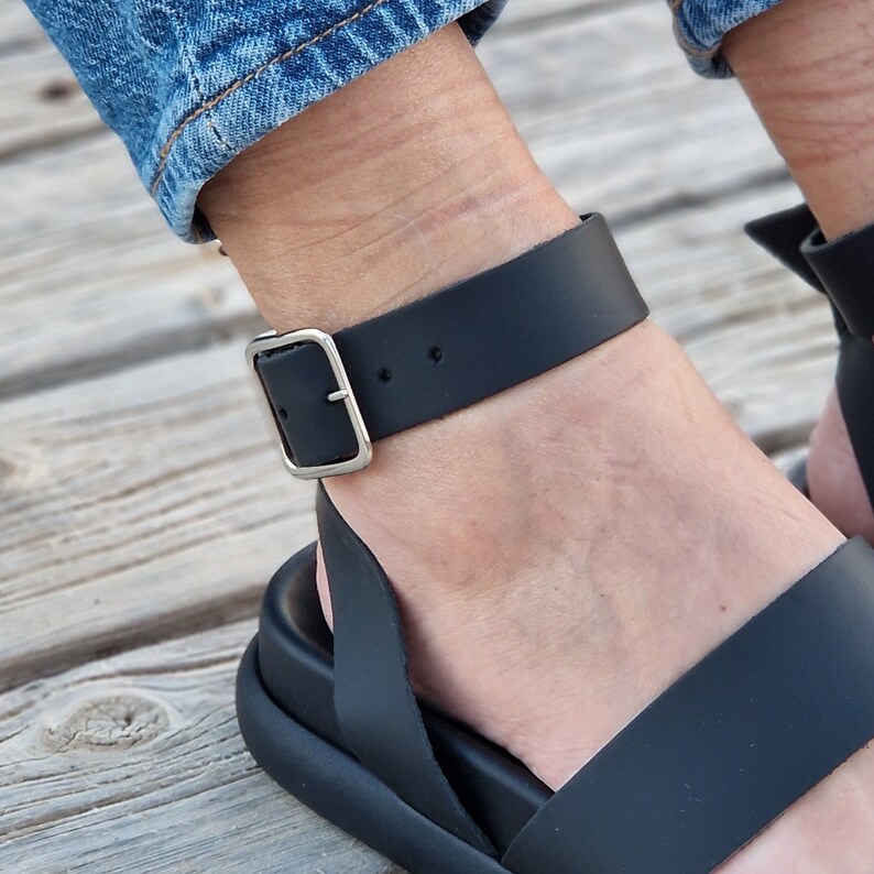 May include: Black leather sandals with a buckle ankle strap. The sandals have a thick platform sole.