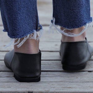 May include: A pair of black leather slip-on shoes with frayed denim jeans.