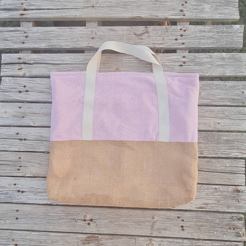 May include: A pink and brown tote bag with white straps. The bag is made of a soft, fuzzy material on the top half and a woven material on the bottom half.