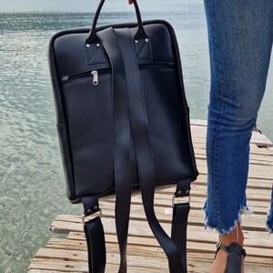May include: A black leather backpack with adjustable straps and a zippered pocket on the front.