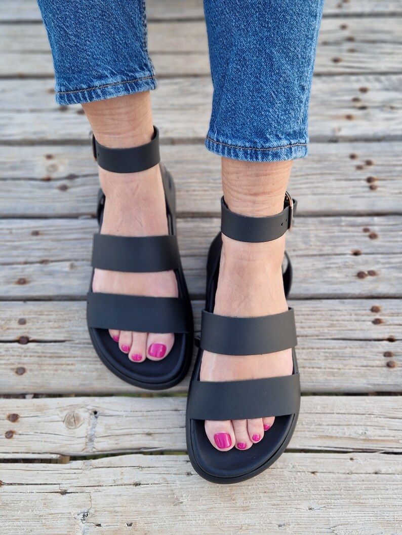 May include: A pair of black leather sandals with two straps across the foot and an ankle strap. The sandals have a chunky platform sole.