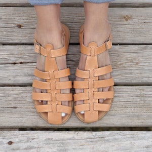 Puede incluir: Un par de sandalias de cuero marrón con un diseño tejido. Las sandalias tienen un cierre de hebilla y se llevan en los pies.