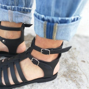 May include: Black leather sandals with a woven design and adjustable ankle straps. The sandals have a flat sole and are made of high-quality leather.