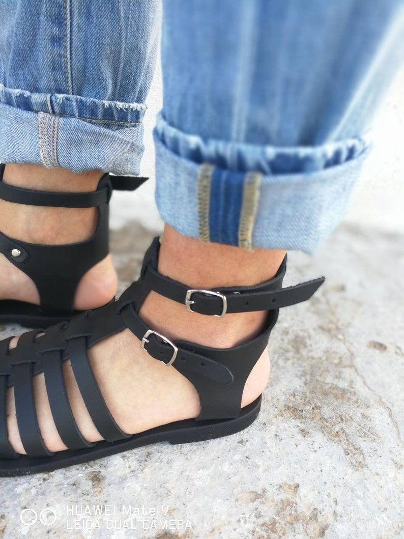 May include: Black leather sandals with a woven design and adjustable ankle straps. The sandals have a flat sole and are made of high-quality leather.