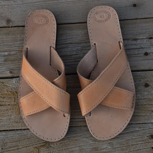 May include: A pair of tan leather sandals with criss-cross straps. The sandals have a simple design and are made of high-quality leather.