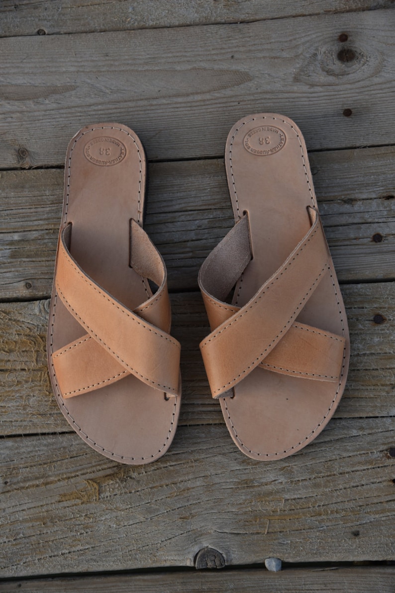 May include: A pair of tan leather sandals with criss-cross straps. The sandals have a simple design and are made of high-quality leather.