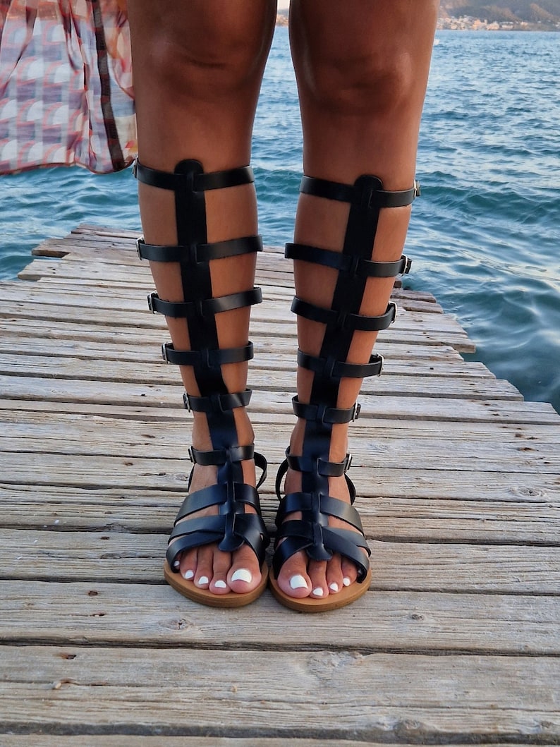 Op de afbeelding: Zwarte gladiatorsandalen van leer met meerdere banden en gespen. De sandalen hebben een gesloten neus en een dikke zool.