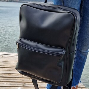 May include: A black leather backpack with a zippered front pocket. The backpack has adjustable straps and a top handle.