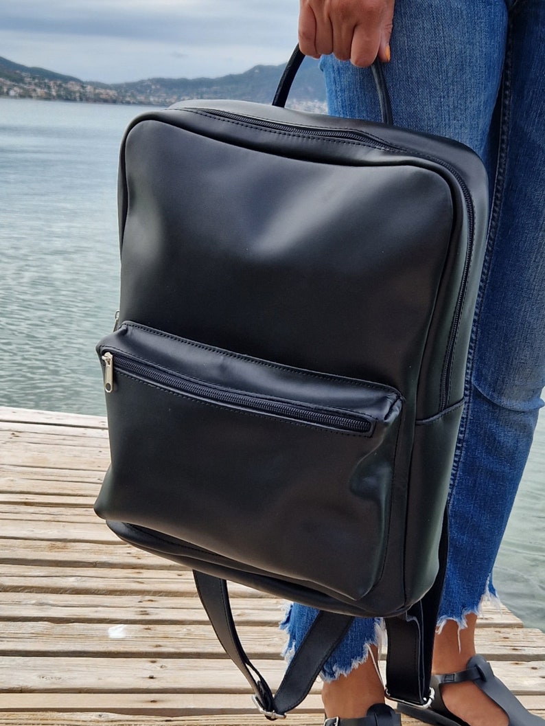 May include: A black leather backpack with a zippered front pocket. The backpack has adjustable straps and a top handle.