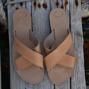 May include: A pair of tan leather sandals with criss-cross straps. The sandals have a simple design and are made of high-quality leather.