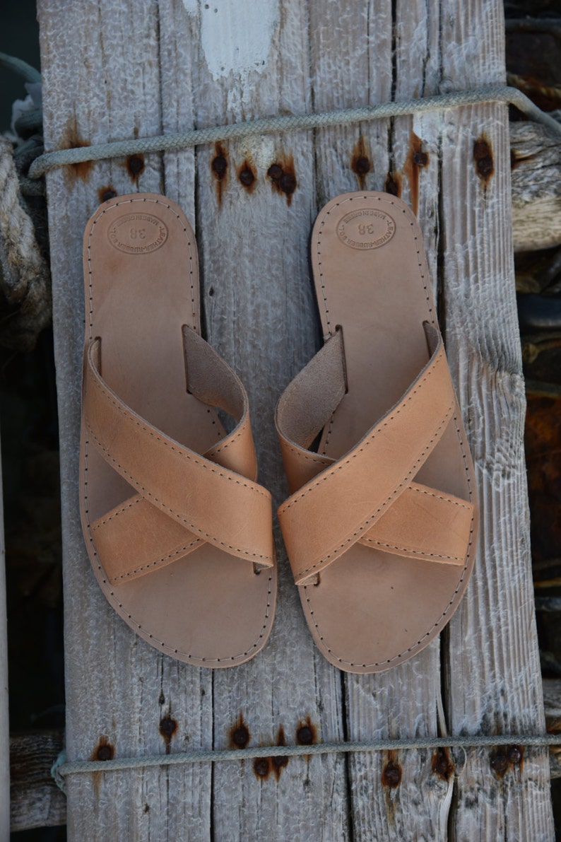 May include: A pair of tan leather sandals with criss-cross straps. The sandals have a simple design and are made of high-quality leather.