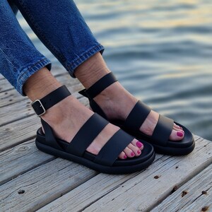 May include: Black leather sandals with two straps and an adjustable ankle strap. The sandals have a thick platform sole.
