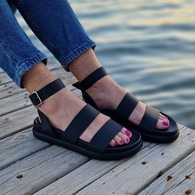 May include: Black leather sandals with two straps and an adjustable ankle strap. The sandals have a thick platform sole.