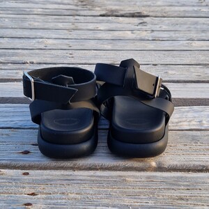 May include: A pair of black leather sandals with adjustable straps and buckles. The sandals have a thick platform sole.