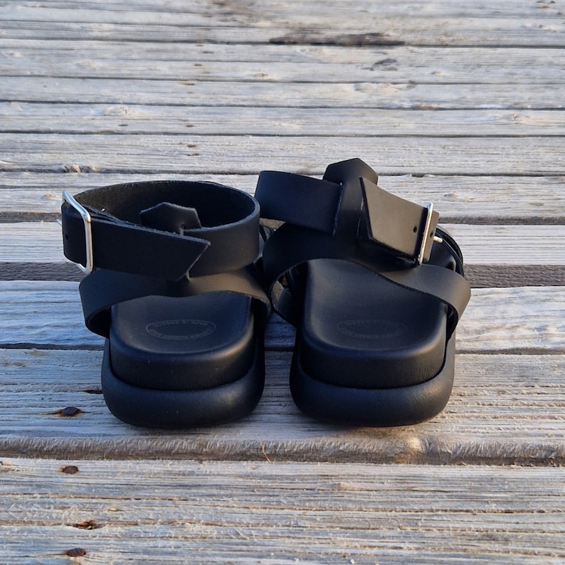 May include: A pair of black leather sandals with adjustable straps and buckles. The sandals have a thick platform sole.