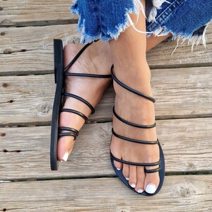 May include: Black leather sandals with multiple straps wrapping around the ankles and feet. The sandals have a simple design and are made of high-quality leather.