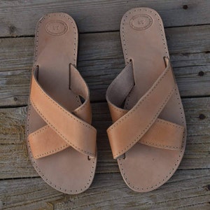 May include: A pair of tan leather sandals with criss-cross straps. The sandals have a simple design and are made of high-quality leather.