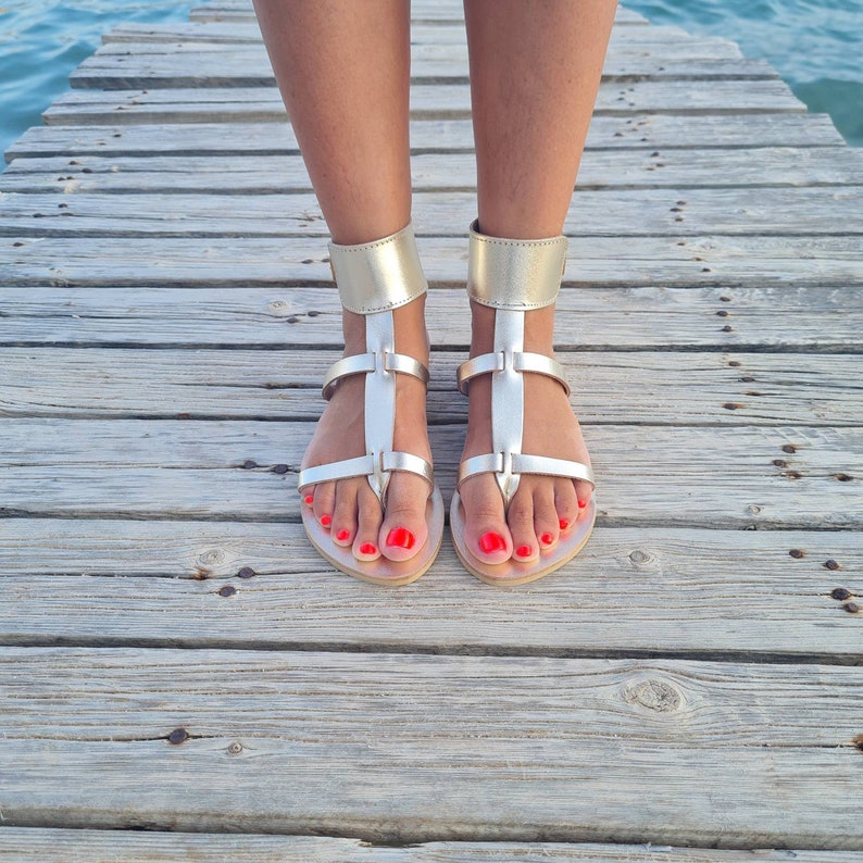 May include: A pair of silver sandals with a criss-cross strap design and red nail polish on the toes.