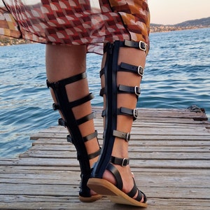 Op de afbeelding: Zwarte leren gladiatorsandalen met meerdere banden en gespen. De sandalen hebben een rits aan de achterkant en een houten plateauzool.
