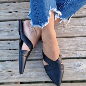May include: A pair of black leather pointed-toe flats with criss-cross straps. The flats are worn by a person with denim jeans.