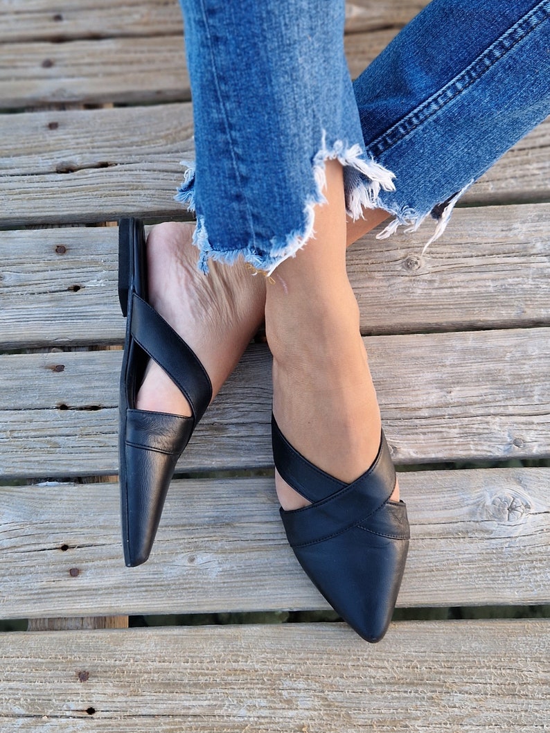 May include: A pair of black leather pointed-toe flats with criss-cross straps. The flats are worn by a person with denim jeans.