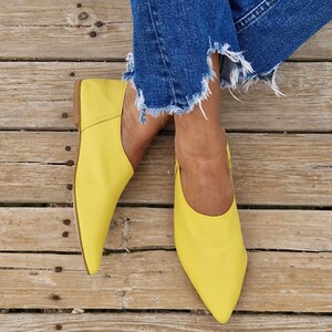 May include: A pair of bright yellow leather flats with pointed toes. The shoes are worn by a person wearing blue jeans.