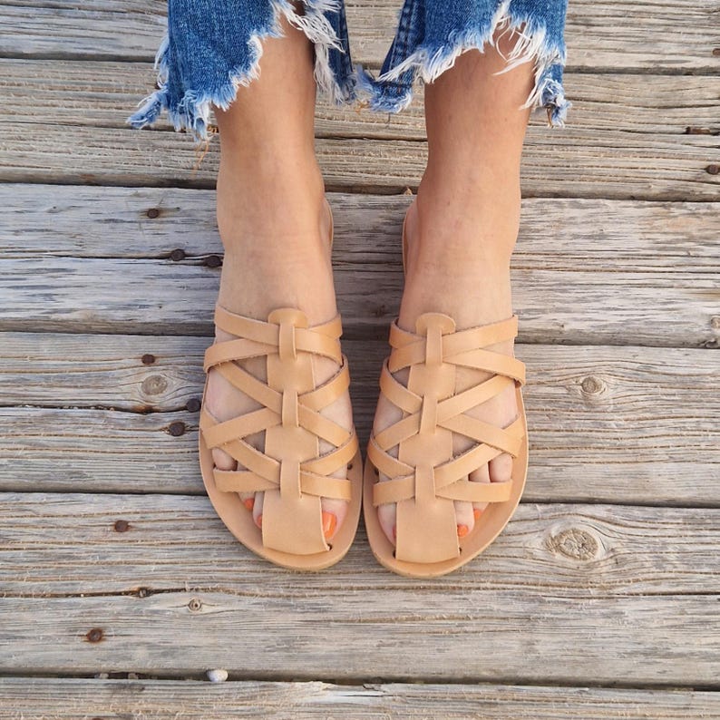 May include: Tan leather sandals with a woven design. The sandals have a flat sole and an open toe.