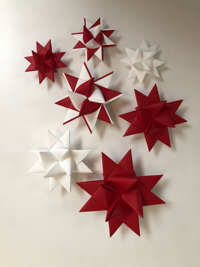 May include: A collection of red and white paper star ornaments. The stars are in various sizes and designs, with some featuring alternating red and white sections. These decorative stars are ideal for holiday or festive decor.