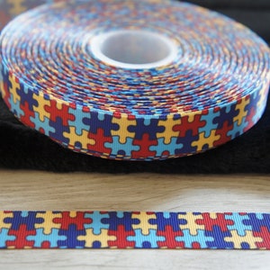 Może przedstawiać: Rolka niebieskiej, czerwonej, ż&oacute;łtej i białej wstążki z wzorem puzzli.