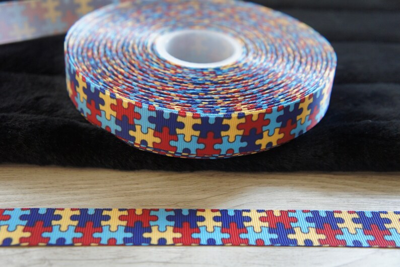 Może przedstawiać: Rolka niebieskiej, czerwonej, ż&oacute;łtej i białej wstążki z wzorem puzzli.